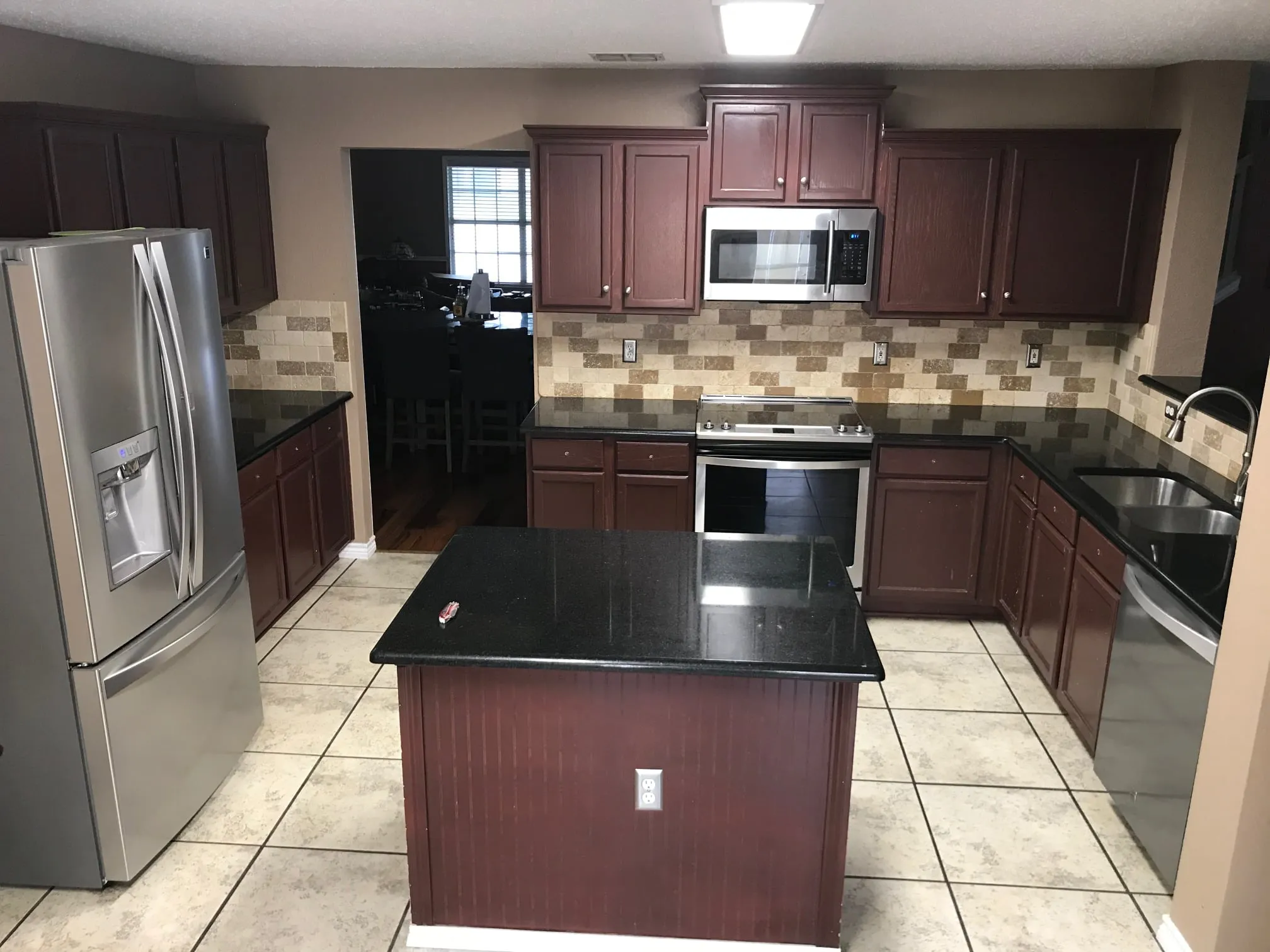 Kitchen with dark reddish-brown cabinets, black countertops, and a beigebrown checkered tile backsplash