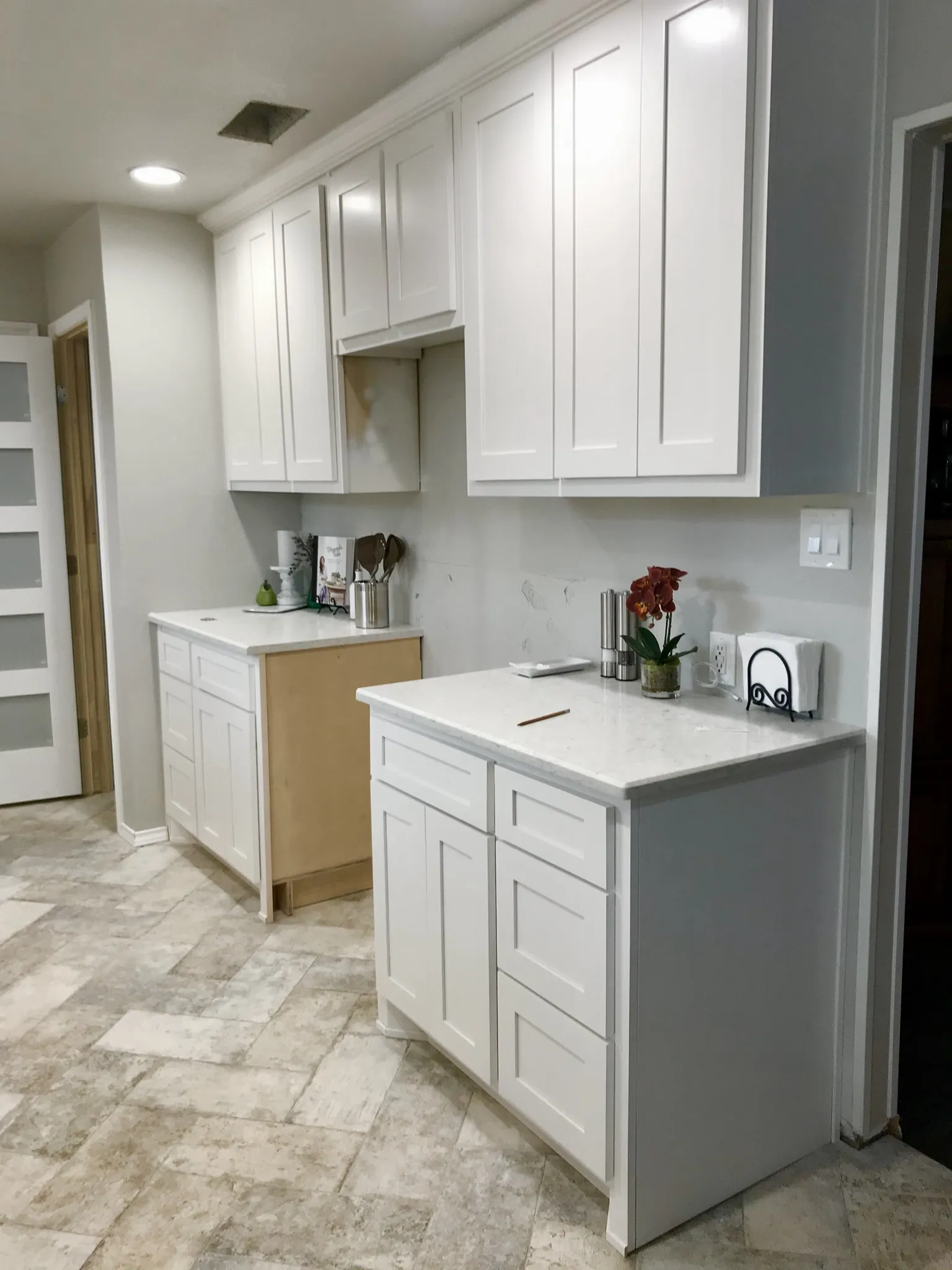 White shaker-style cabinets and light marble-look countertops in a kitchen undergoing renovation, with a patterned light gray floor tile