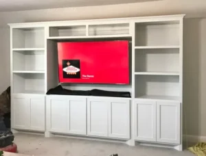 Built-in white entertainment center with shelving and cabinets surrounding a mounted television