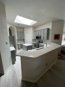 Full view of a remodeled kitchen with gray cabinets, curved bar seating, a skylight, and a small central island