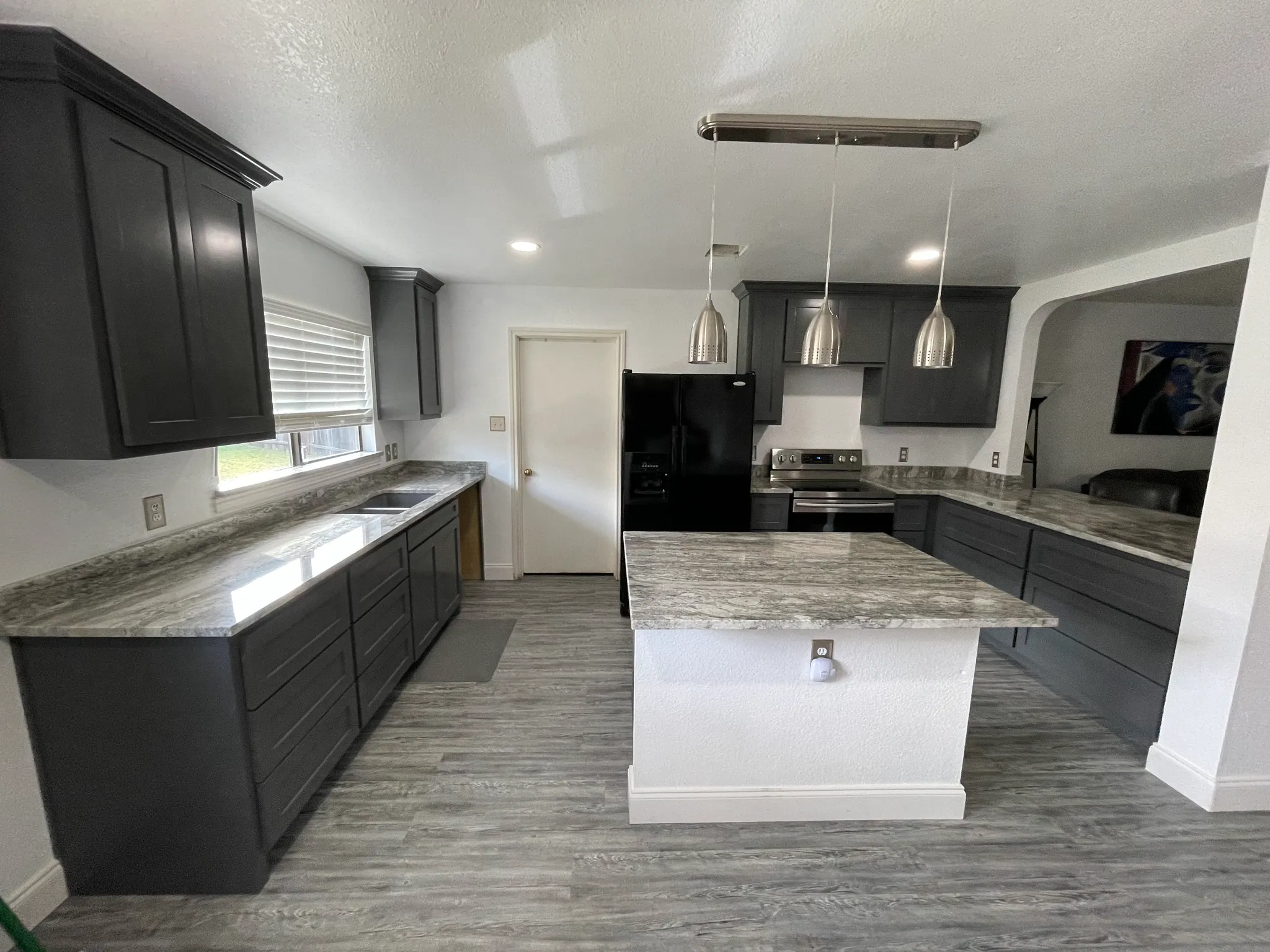 Modern kitchen featuring gray cabinets, a marble countertop, stainless steel appliances, and pendant lighting over the central island
