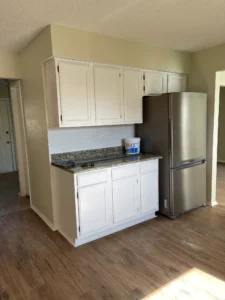 Small kitchen area with white cabinets, granite countertop, a stainless steel refrigerator, and wood flooring