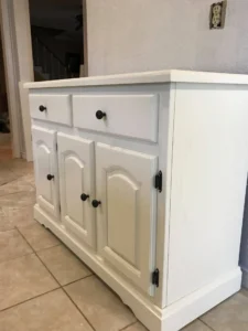 White painted buffet cabinet with arched lower doors and black knobs sitting on a tiled floor